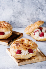 Homemade choux pastry cake Paris Brest with raspberries, almond and rosemary, served on wooden serving board over gray blue texture background. French dessert