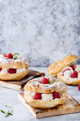 Homemade choux pastry cake Paris Brest with raspberries, almond, sugar powder and rosemary, served on wooden serving board over gray blue texture background. French dessert