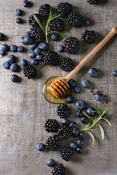 Berries blackberry and blueberry, honey on dipper, rosemary served over gray metal texture background. Summer appetizer. Top view with space