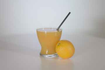 A lemon is standing on a table next to a glass with juice.