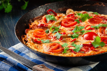 Frittata made of eggs, sausage chorizo, red pepper, green pepper, tomatoes, cheese and chili in a pan on wooden table