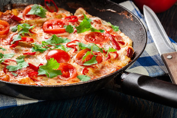 Frittata made of eggs, sausage chorizo, red pepper, green pepper, tomatoes, cheese and chili in a pan on wooden table