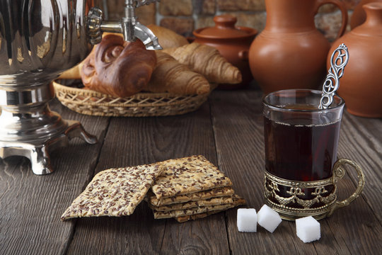 A glass of tea with cracker and buns near the samovar. Retro stylized photo