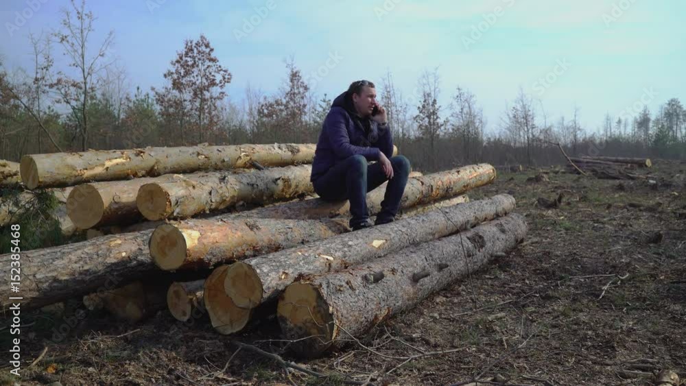 Aufkleber a man sits on logs and calls by phone when ordering a car for transporting timber 4k video