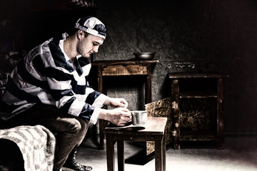 Male prisoner wearing prison uniform sitting on a bed and eating from aluminum dishes