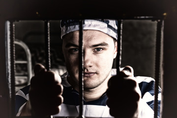 View through iron door with prison bars on young prisoner holding bars in a jail cell