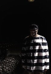 Aggressive male prisoner standing near his bed in a small dark prison cell