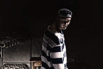 Prisoner with an angry look standing near his bed in a small dark prison cell