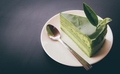 Close up Green tea cake on white disk with matcha green tea on the black wooden, sweet food of dessert Green tea cake. background space for texture.