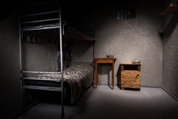 Jail cell with iron bunk bed and wooden bedside table