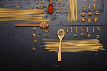 Pasta and spices in wooden spoons put on grey surface