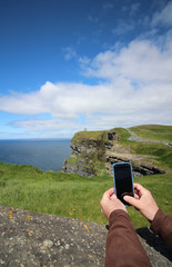 Hands holding phone at tourist location Cliffs of Moher