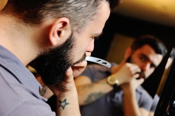 Barber or a hairdresser cuts hair and beard to a man in a hairdresser or a barbershop