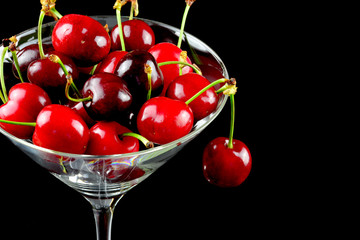 Kirschen im Cocktailglas vor schwarzem Hintergrund mit Textfreifeld