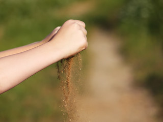 Child's hands pouring the sand on summer nature background