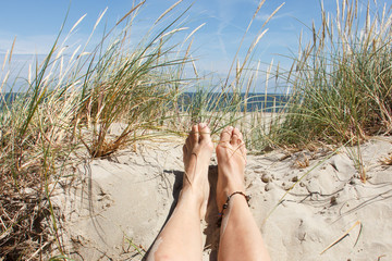 Lady's feet lying in the sand on a dune on a sunny day on the island of Texel, The Netherlands. - obrazy, fototapety, plakaty