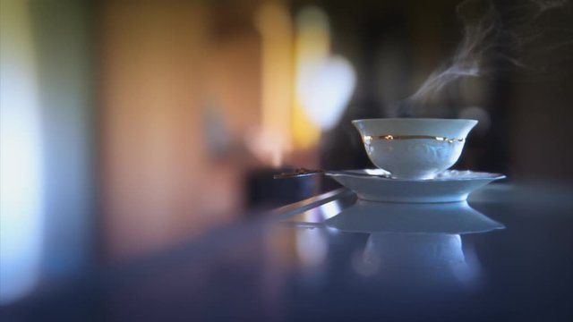 Vintage porcelain teacup with hot tea on a glass desktop. Blue tint.