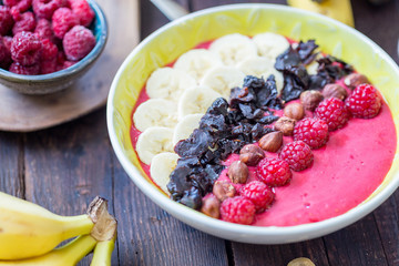 Breakfast Raspberry Smoothie Bowl topped with Raspberries, Banana, Prunes and Hazelnuts on Dark Wooden Table, Horizontal View