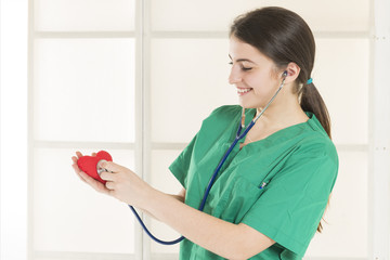 Female doctor examining a red heart with a stethoscope. Healthy lifestyle, healthcare and medicine concept. Professional care for your heart. Checkup your heart