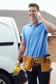 Electrician With Van Talking On Mobile Phone Outside House