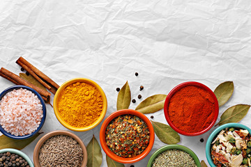 Spices in colorful bowls viewed from above. Various seasonings on a white background. Italian mix, cumin, chili pepper, curry powder, salt, pepper, garlic, cinnamon tomato. Top view. Copy space