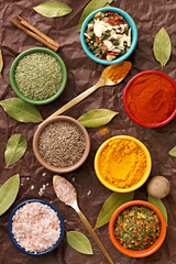 Spices in colorful bowls viewed from above. Various seasonings on a dark background. Italian mix, cumin, chili pepper, curry powder, Himalayan salt, pepper, garlic, cinnamon, dried tomato. Top view