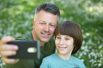 Father and son taking photo with smartphone together outdoor. Family selfie time.