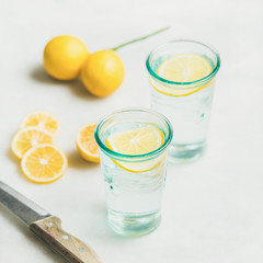 Morning detox lemon water in glasses and fresh lemons over marble background, selective focus, square crop. Clean eating, weight loss, healthy, detox, dieting concept