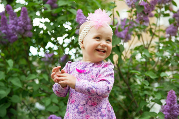 Beautiful little girl happy smiling and claps her hands over lilac flowers in spring park. Childhood. Cute kid's face over nature background. Cheerful child's portrait, soft focus.