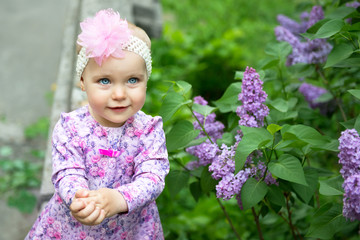 Beautiful little girl happy smiling and claps her hands over lilac flowers in spring park. Childhood. Cute kid's face over nature background. Cheerful child's portrait, soft focus.