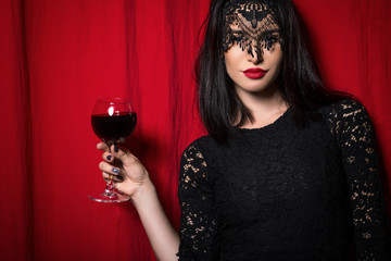 Young beautiful woman holding glass of wine over red curtains