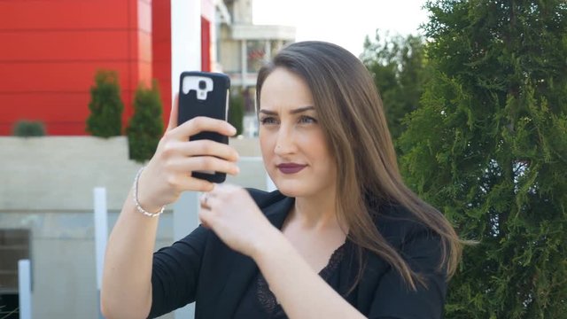 Beautiful woman checking her makeup and hair using camera of smartphone before taking selfie