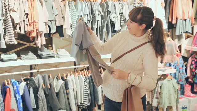 
Pregnant woman deciding on clothes for baby in children clothes shop