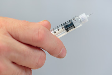 Insulin injection. The hand of a man holding an insulin pen, on gray background