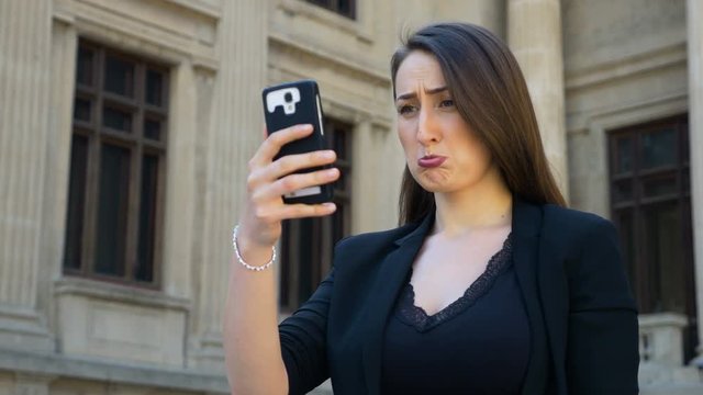 Portrait of a woman holding a smartphone and taking selfies videos making sad face