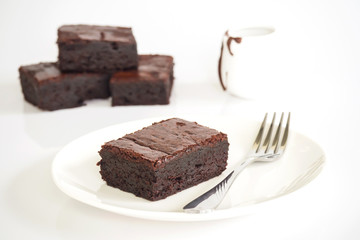 Sliced brownies on white plate. Served with chocolate fudge. On white plate over white background....