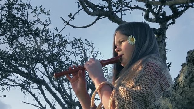 Girl plays a flute sitting on a tree.
