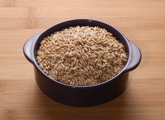 Oat grains in porcelain bowl on wooden rattan bamboo table
