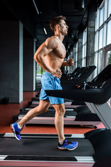 Fototapeta na wymiar Side view full length of young man in sportswear running on treadmill at gym