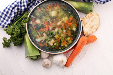 Broth with carrots, onions various fresh vegetables in a pot - colorful fresh clear spring soup. Rural kitchen scenery vegetarian bouillon or stock
