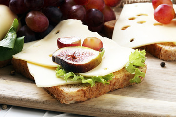 Bread with slices of cheese, some grapes and fig for lunch table. Sharing antipasti on party or summer picnic time