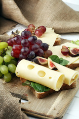 Bread with slices of cheese, some grapes and fig for lunch table. Sharing antipasti on party or summer picnic time