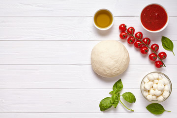 Fototapeta na wymiar Raw pizza dough with baking pastry ingredients: mozzarella, tomatoes sauce, basil, olive oil, cheese, spices.