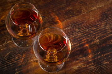 Two snifter wine glasses with cognac or brandy on vintage wooden background. Top view. Copy space for text. 