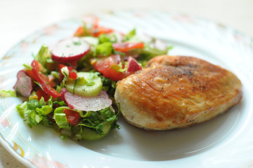 Baked chicken breast with vegetable salad on a white plate