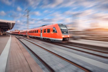 Tuinposter Red modern high speed train in motion on railroad track at sunset in Europe. Train on railway station with motion blur effect. Industrial landscape with train, railway platform and colorful sky © den-belitsky