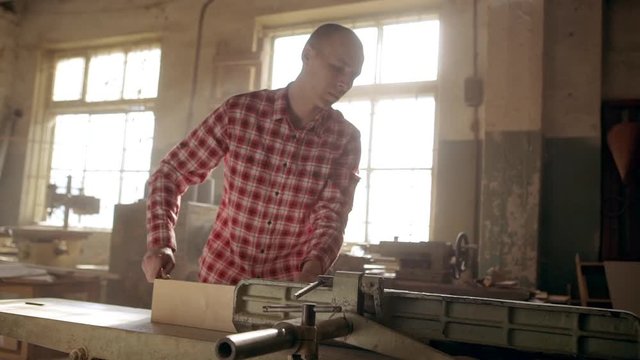 Concentrated Caucasian bolding male in red plaid shirt putting long wood plank on jointer machine in slowmotion