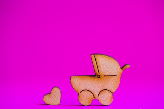 Wooden icon of baby buggy and little heart on crimson background