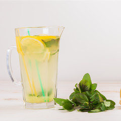 A glass decanter with a summer refreshing lemonade made of lemons and ginger with mint added on a white wooden background. Detox water. Ingredients. Cleaning the body of toxins, vitamins