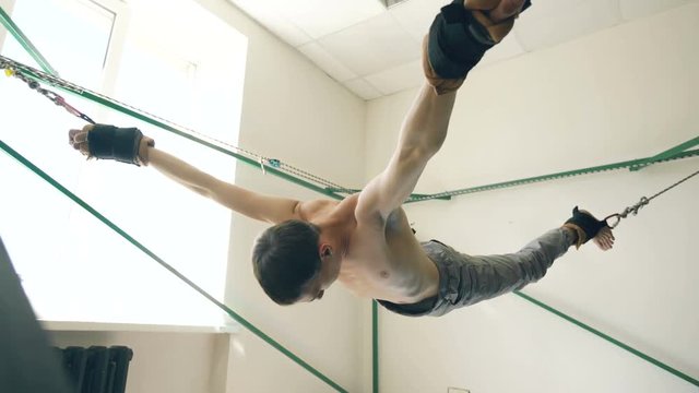 Young man doing exircise on quartering yoga equipment and pull his arms and legs with ropes